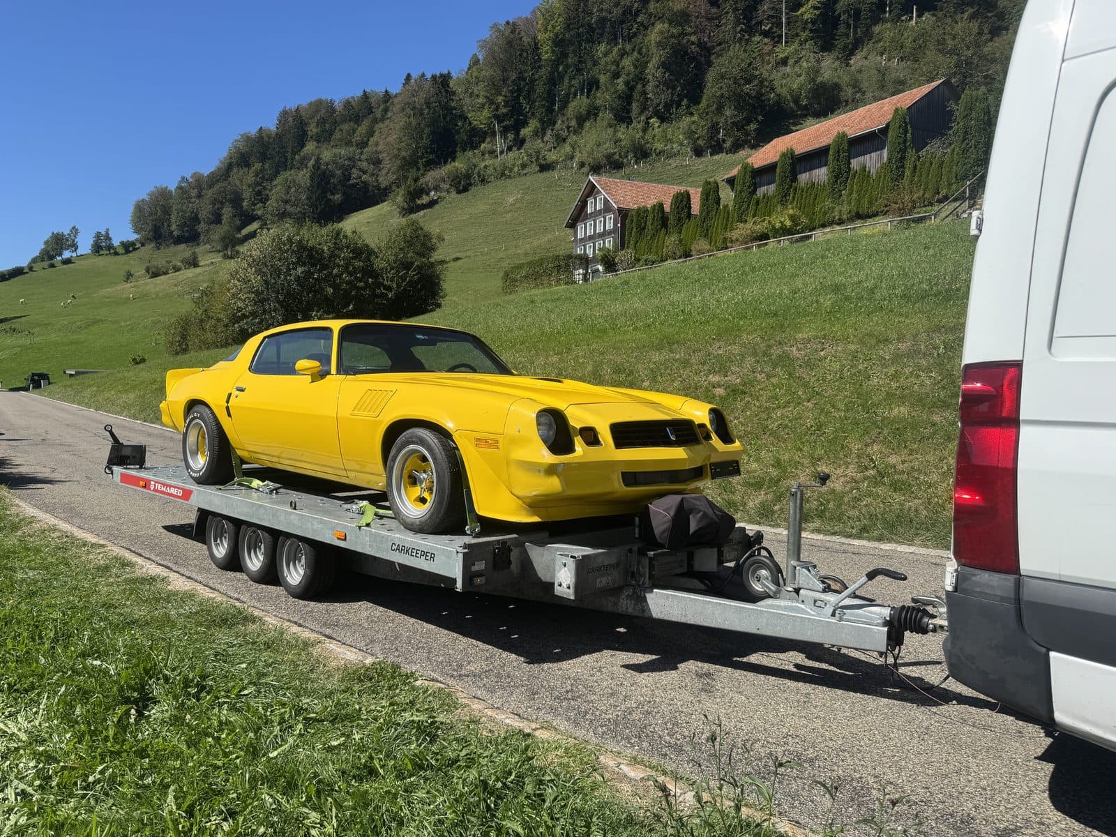 Gelber Oldtimer auf dem Autotransportanhänger, unterwegs auf einer Landstrasse