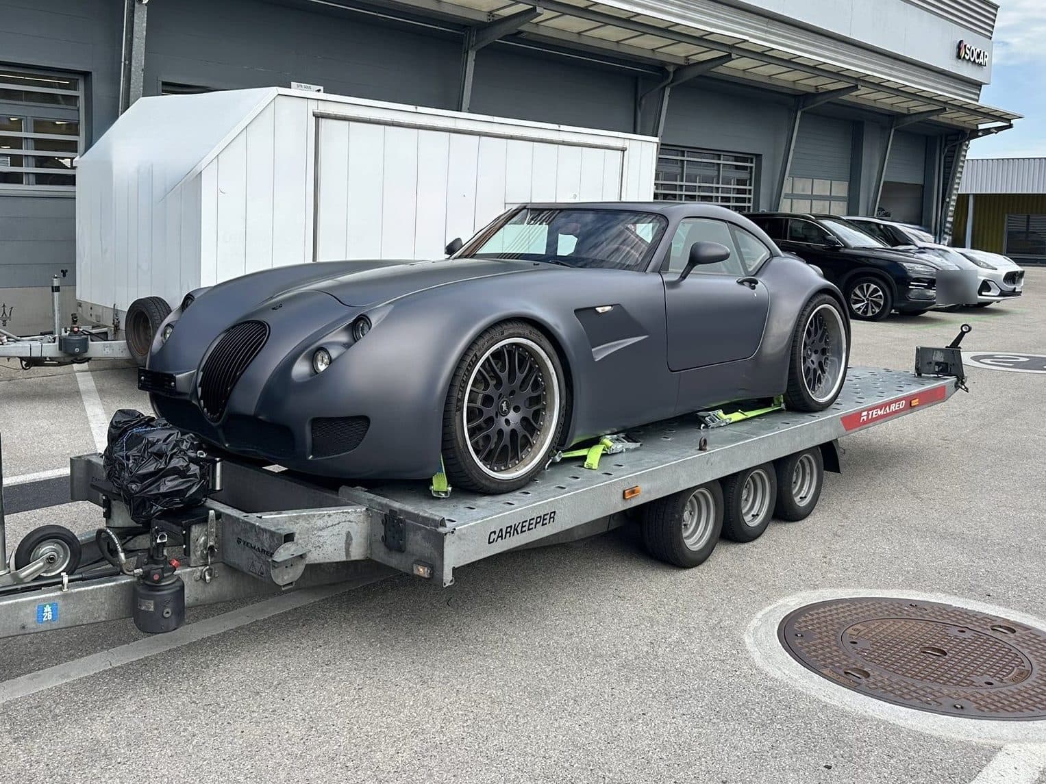 Mattgrauer Sportwagen, auf dem Anhänger mit Spanngurten gesichert